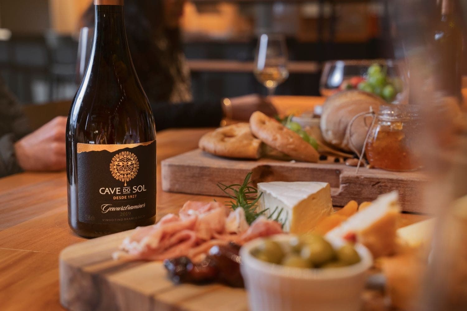 Garrafa de Gewürztraminer Cave do Sol servida em uma mesa com queijos e pães